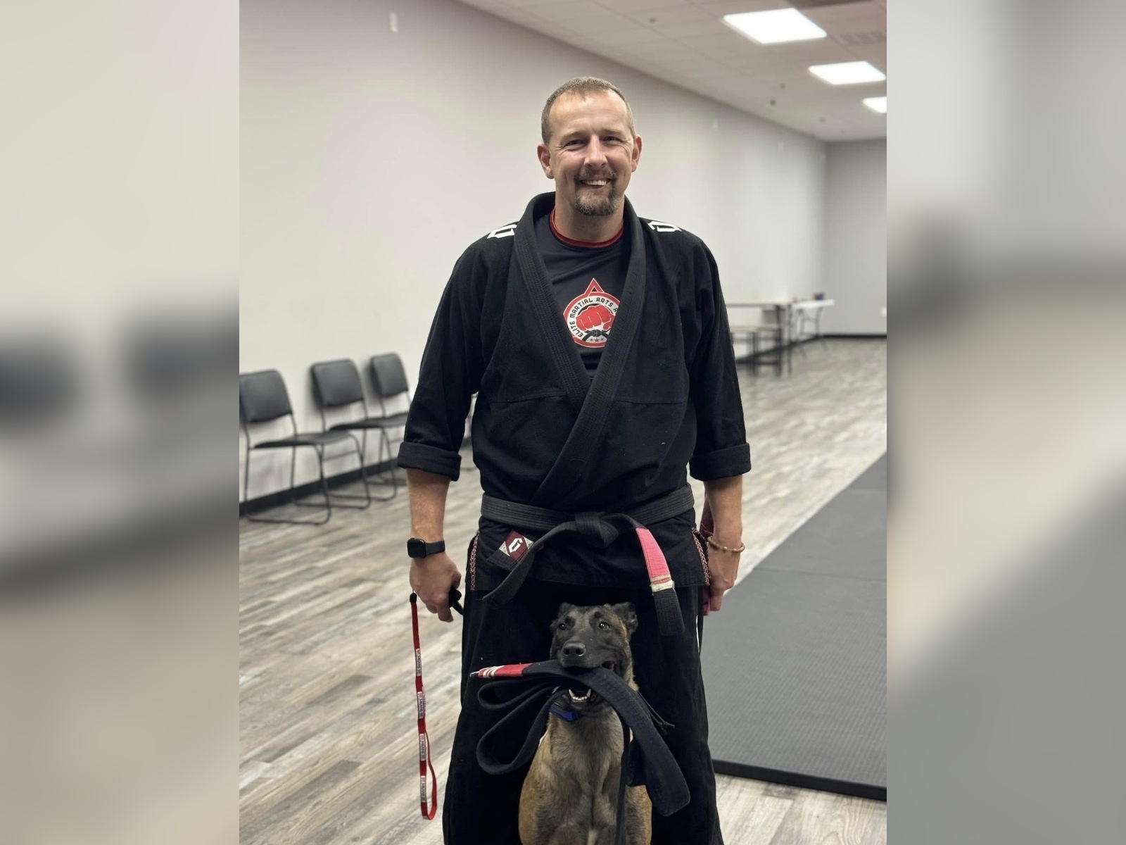 Alan wearing a black Brazilian Jiu-Jitsu gi with a Belgian Malinois holding a black belt